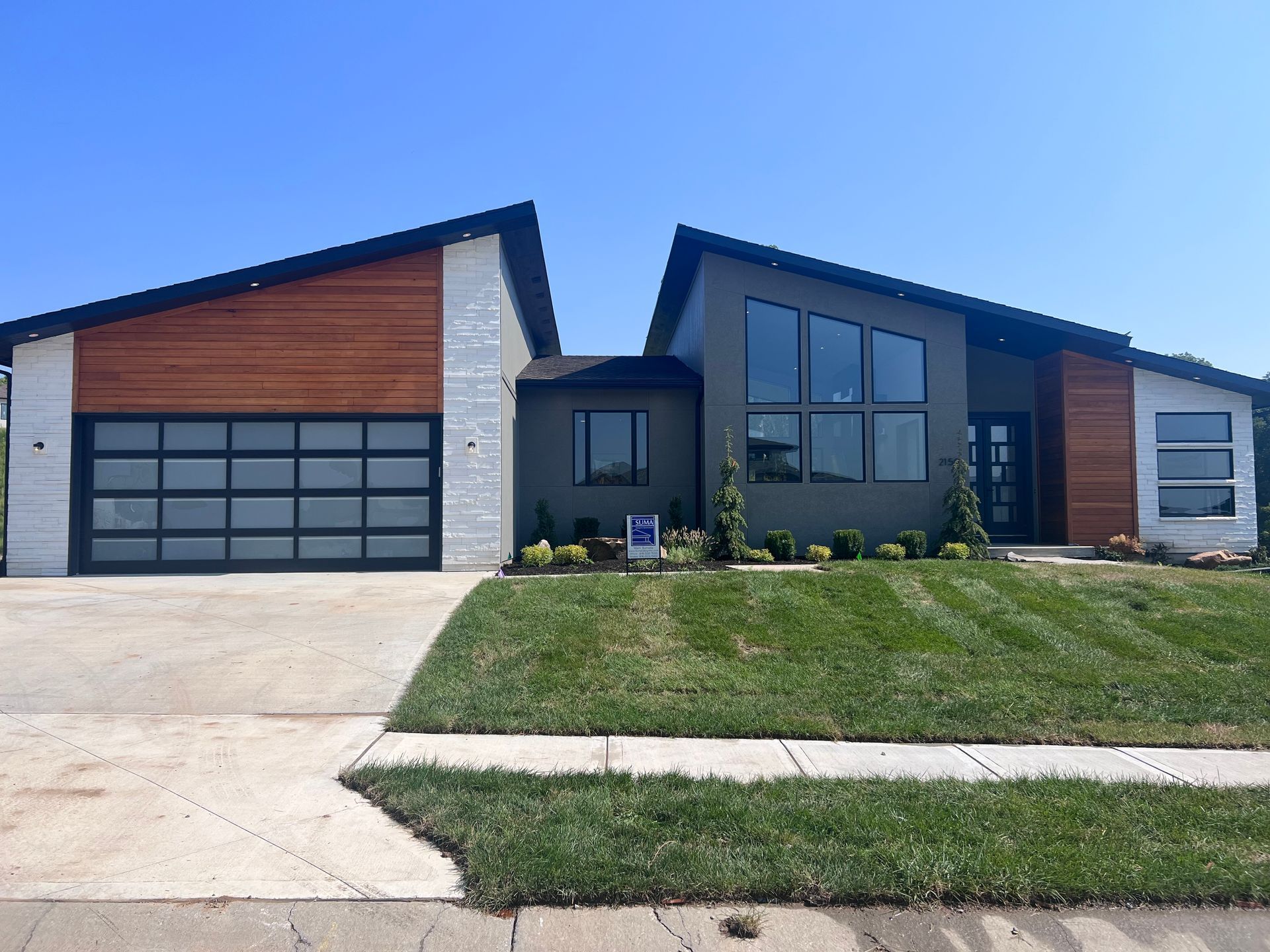 A modern one-story suburban house with a sloped roof, gray exterior, wood paneling, and a white stone garage.