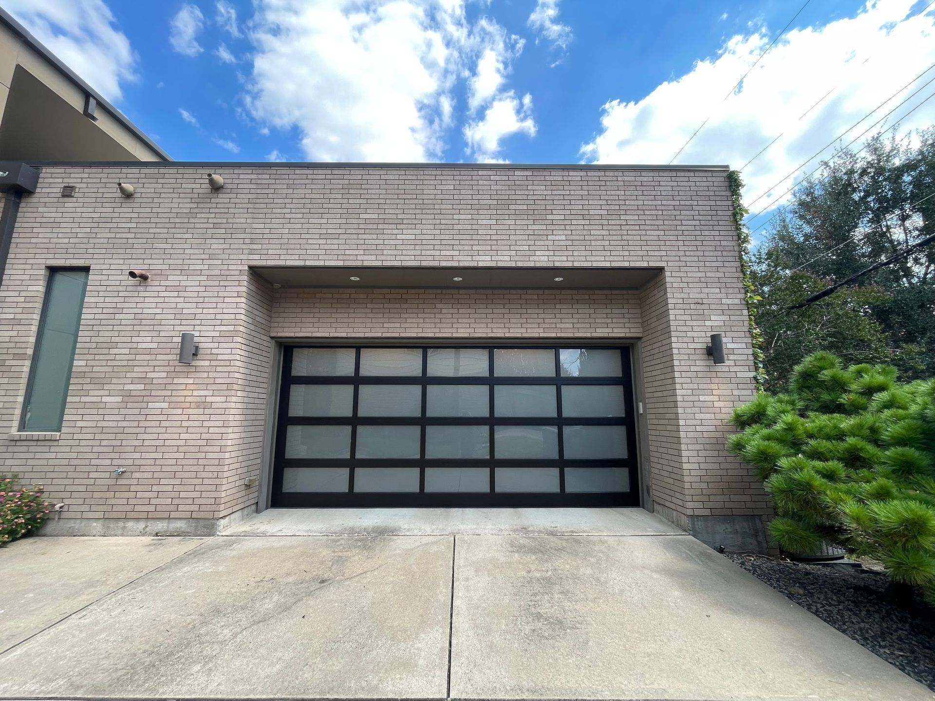 A modern garage exterior with light wood horizontal siding and a large, black-framed frosted glass sectional door.