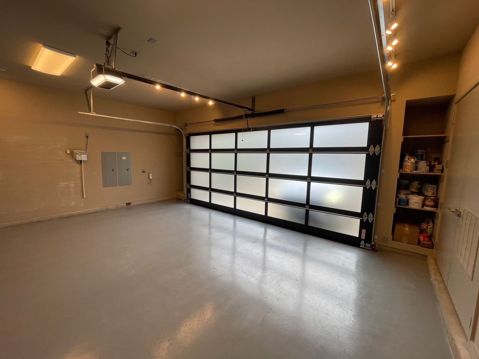 Empty residential garage with a gray epoxy floor, beige walls, and a large, frosted-glass paneled garage door.