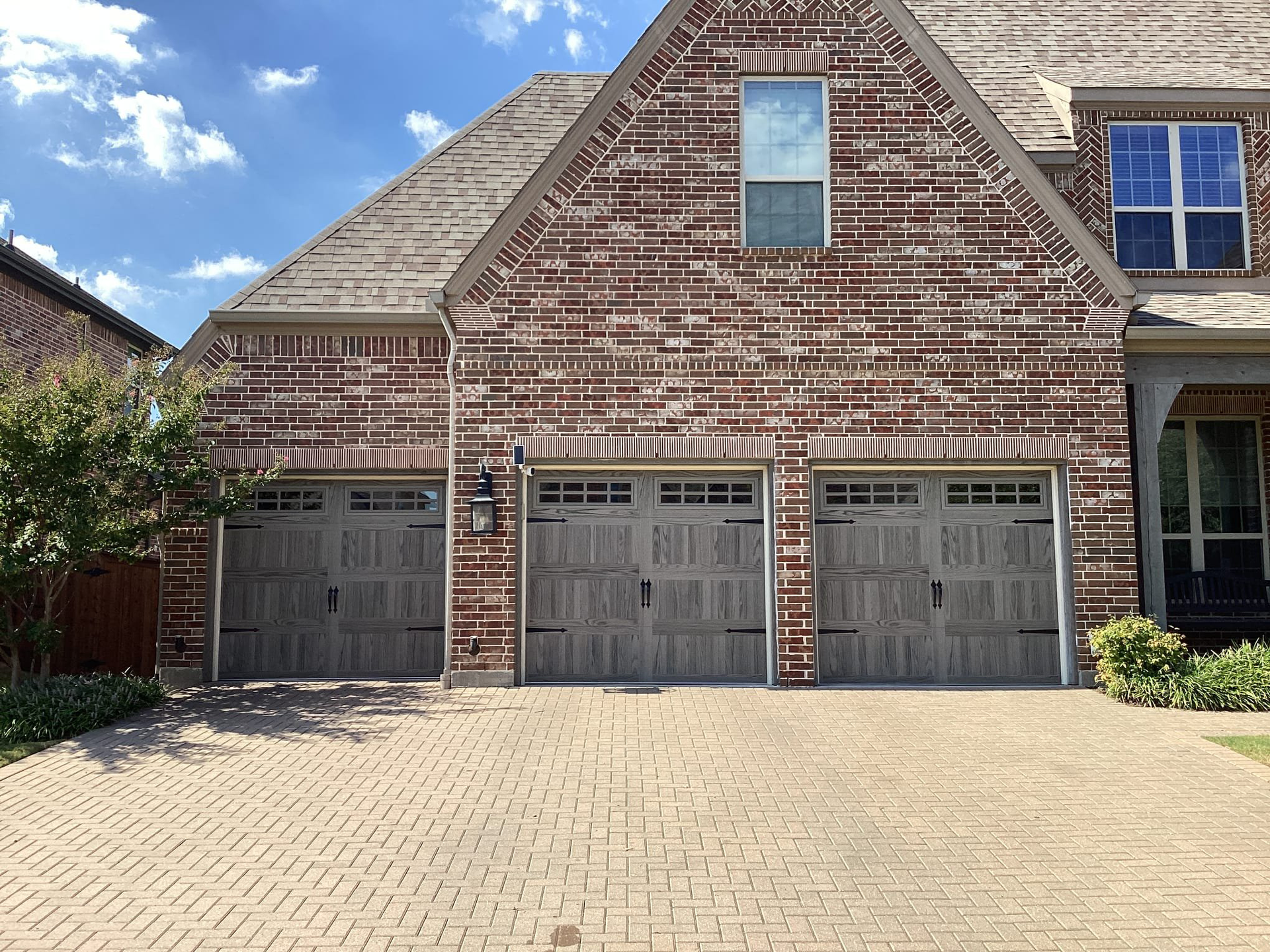 Three-car garage with brick exterior and cobblestone driveway. Garage doors are gray with decorative hardware.