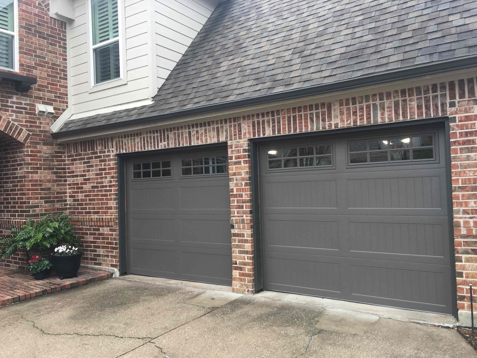A residential two-car garage with dark gray doors and windows, set in a brick and siding home with a concrete driveway.