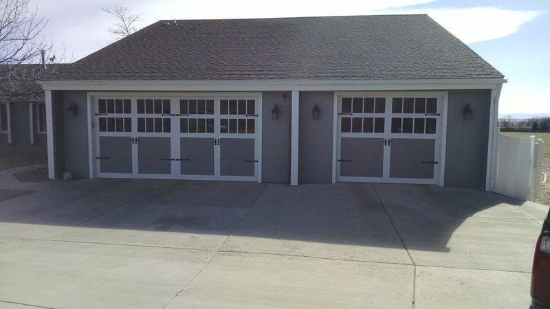 A gray detached three-car garage with white trim and carriage-style doors under a gabled roof on a concrete driveway.