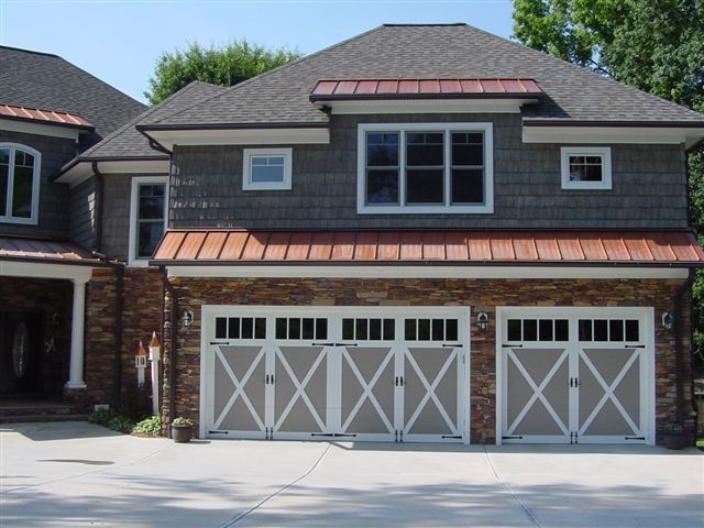 A two-story home with gray shake siding, a stone facade, copper roof accents, and two white carriage-style garage doors.