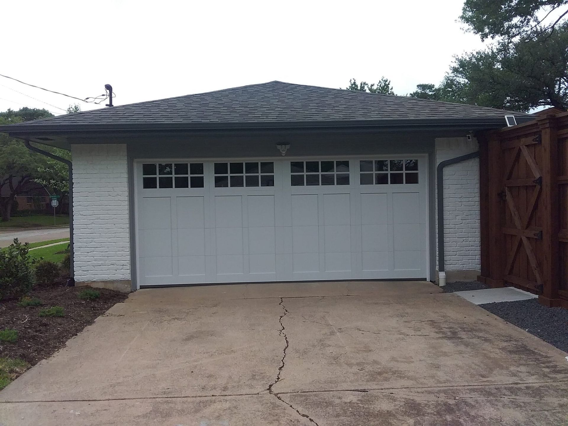 A white garage with a gray shingled roof, windows in the door, and a cracked concrete driveway in front.