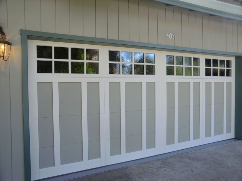 A white multi-panel residential garage door with upper window panes and grey trim accents on the exterior of a building.