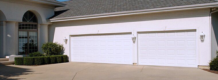 A white suburban house with a two-car garage and a wide concrete driveway.