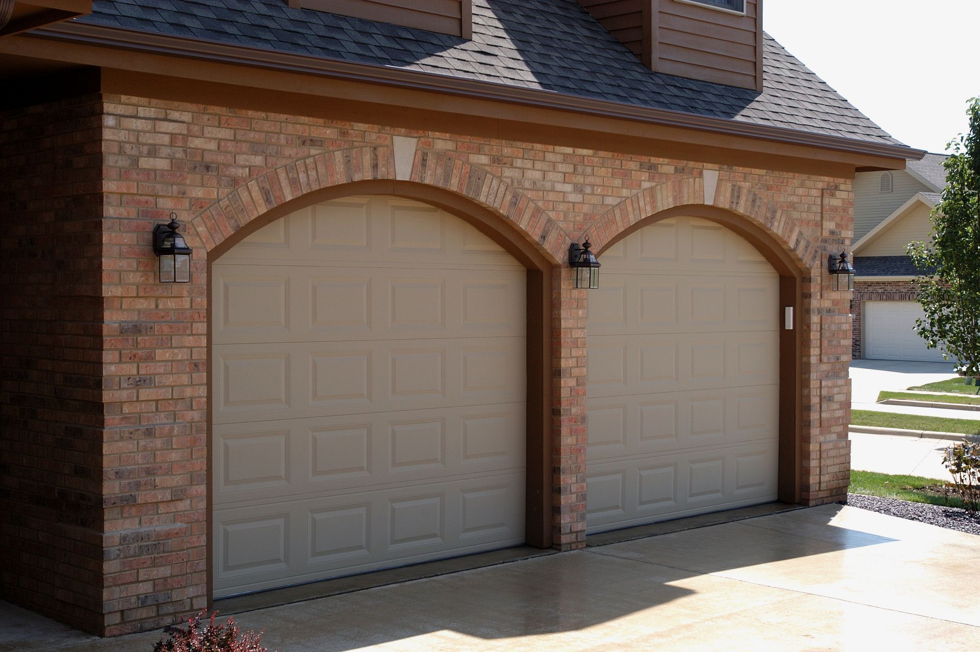 A beige, two-car garage with arched openings set in a brick exterior of a residential home.