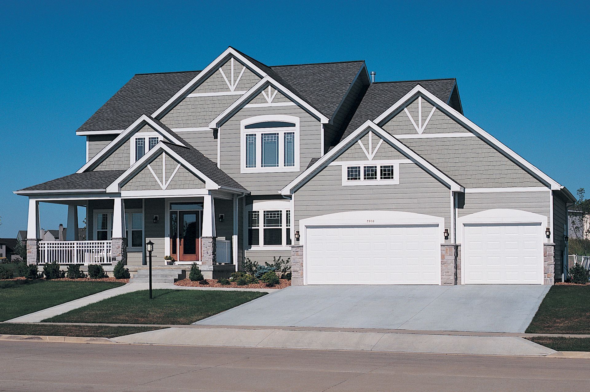 A two-story grey suburban house with a covered front porch, a multi-car garage, and a concrete driveway.