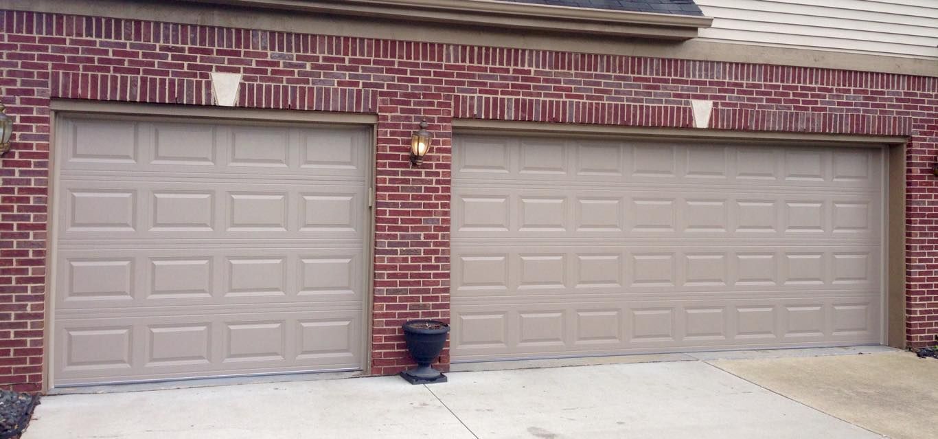 Two tan garage doors set into a red brick house wall, with a small black planter placed between the doors.