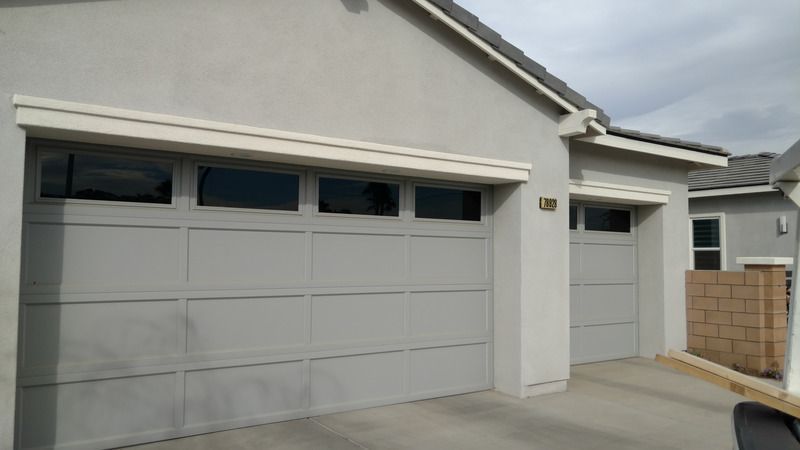 A beige house exterior featuring a wide two-car garage next to a single-car garage, both with upper row windows.