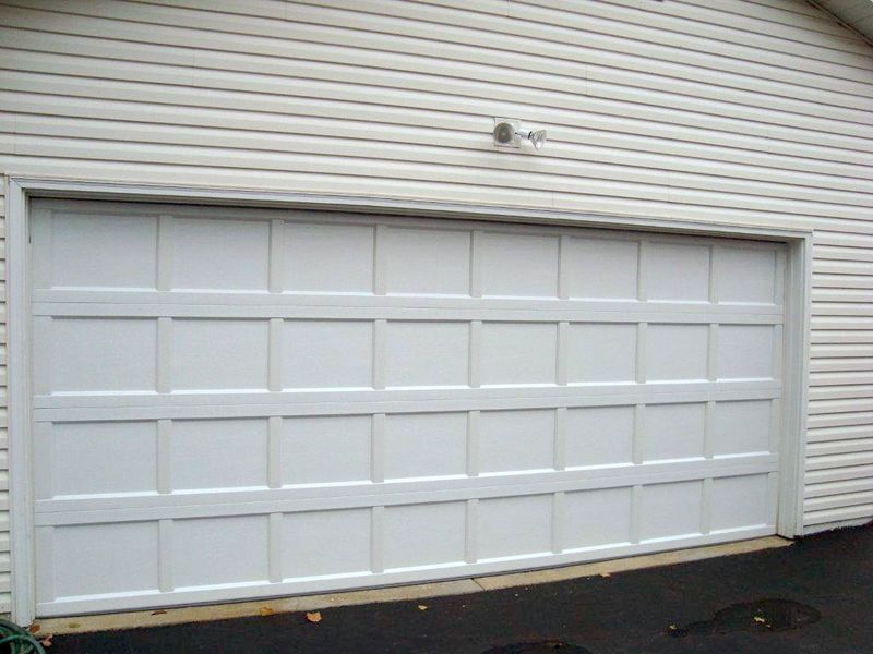 A white, multi-paneled garage door installed on a house with horizontal siding.