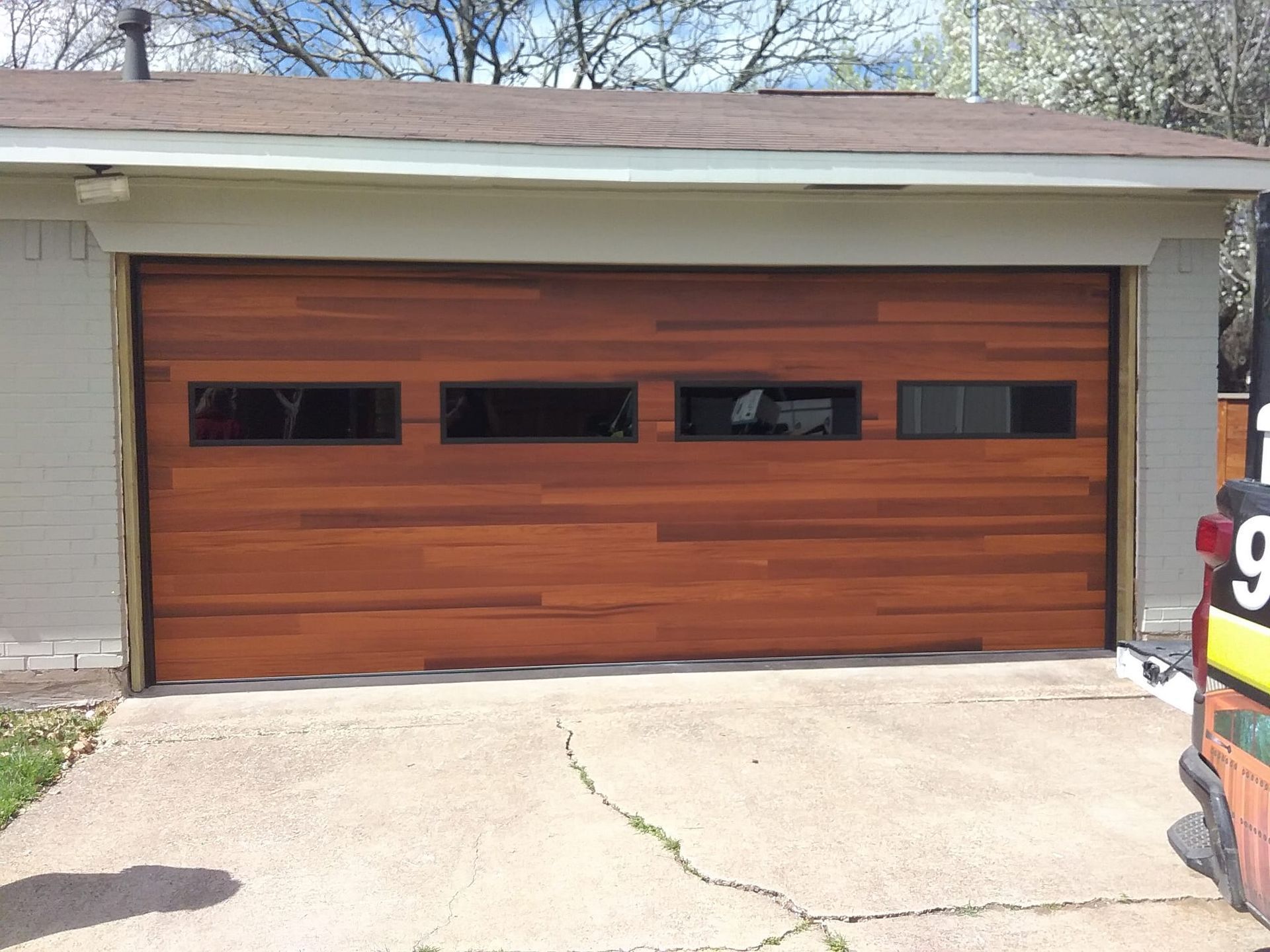 Modern horizontal wood slat garage door with a row of four rectangular windows, mounted on a grey brick building.