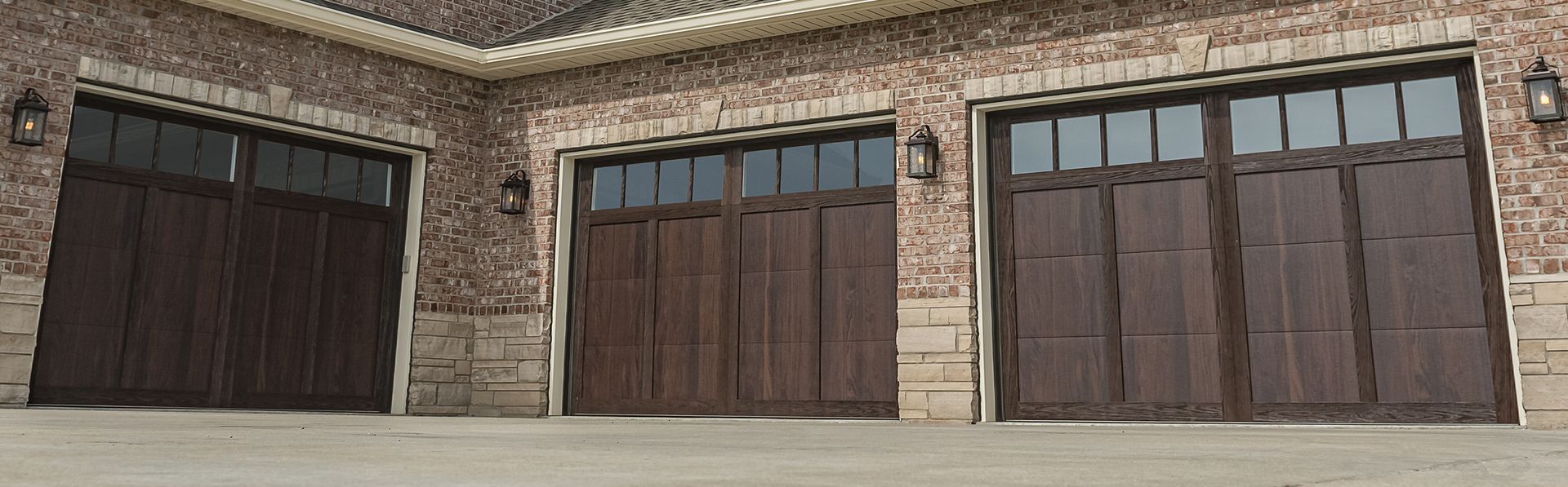 Three dark wood carriage-style garage doors with windows set in a brick and stone exterior wall.