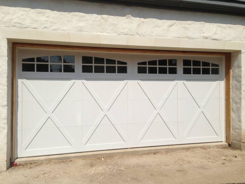 A white carriage-style garage door featuring a decorative X-brace design and an arched row of windows at the top.