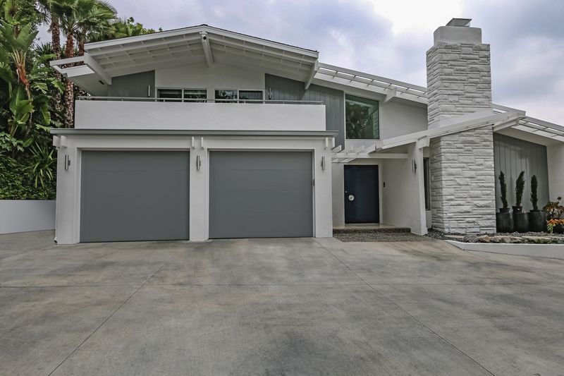 A two-story white suburban house with a gray two-car garage, stone chimney, and a driveway under a cloudy sky.