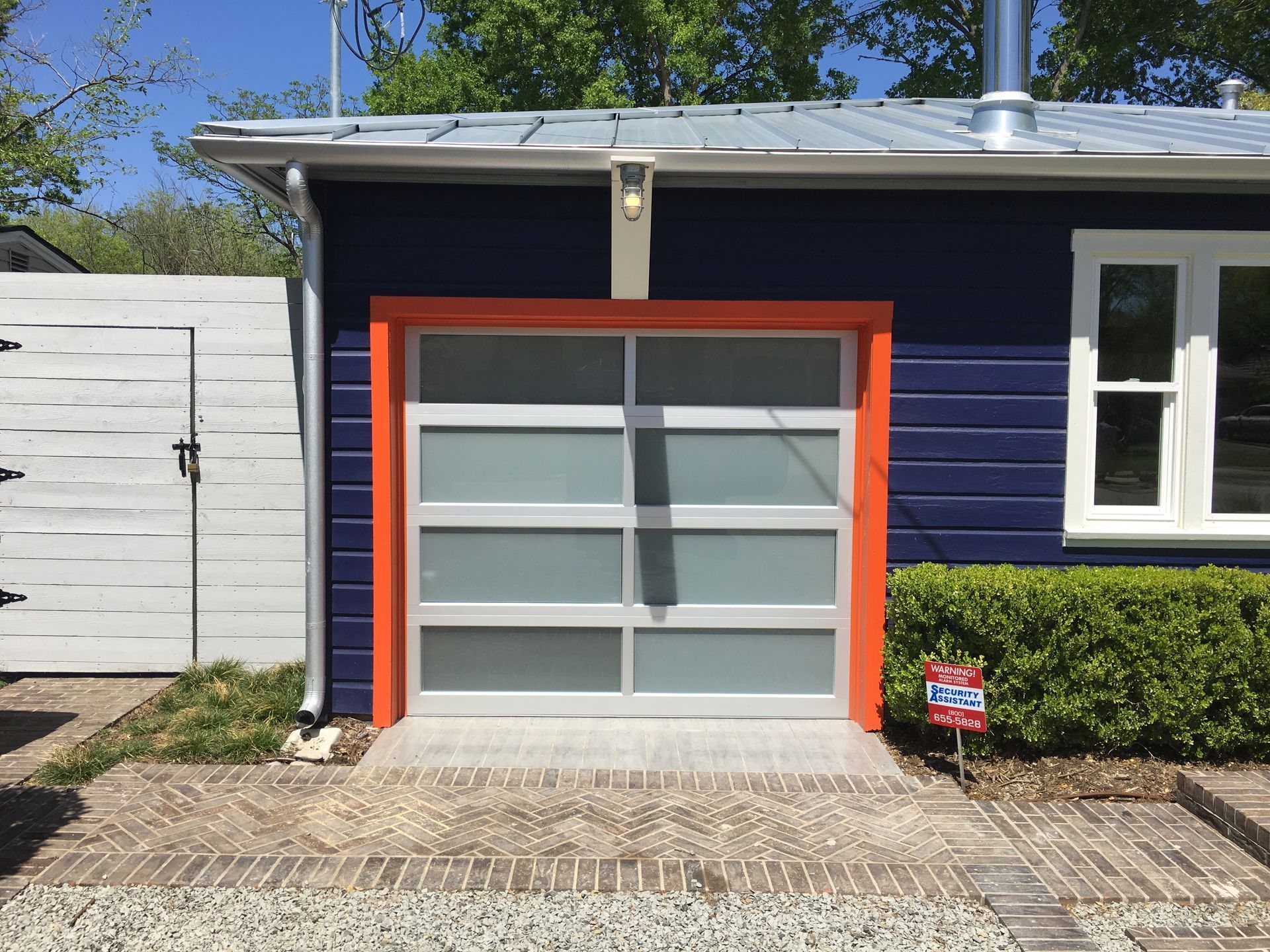 Blue building with orange trimmed garage door; frosted glass, silver frame. Brick path.
