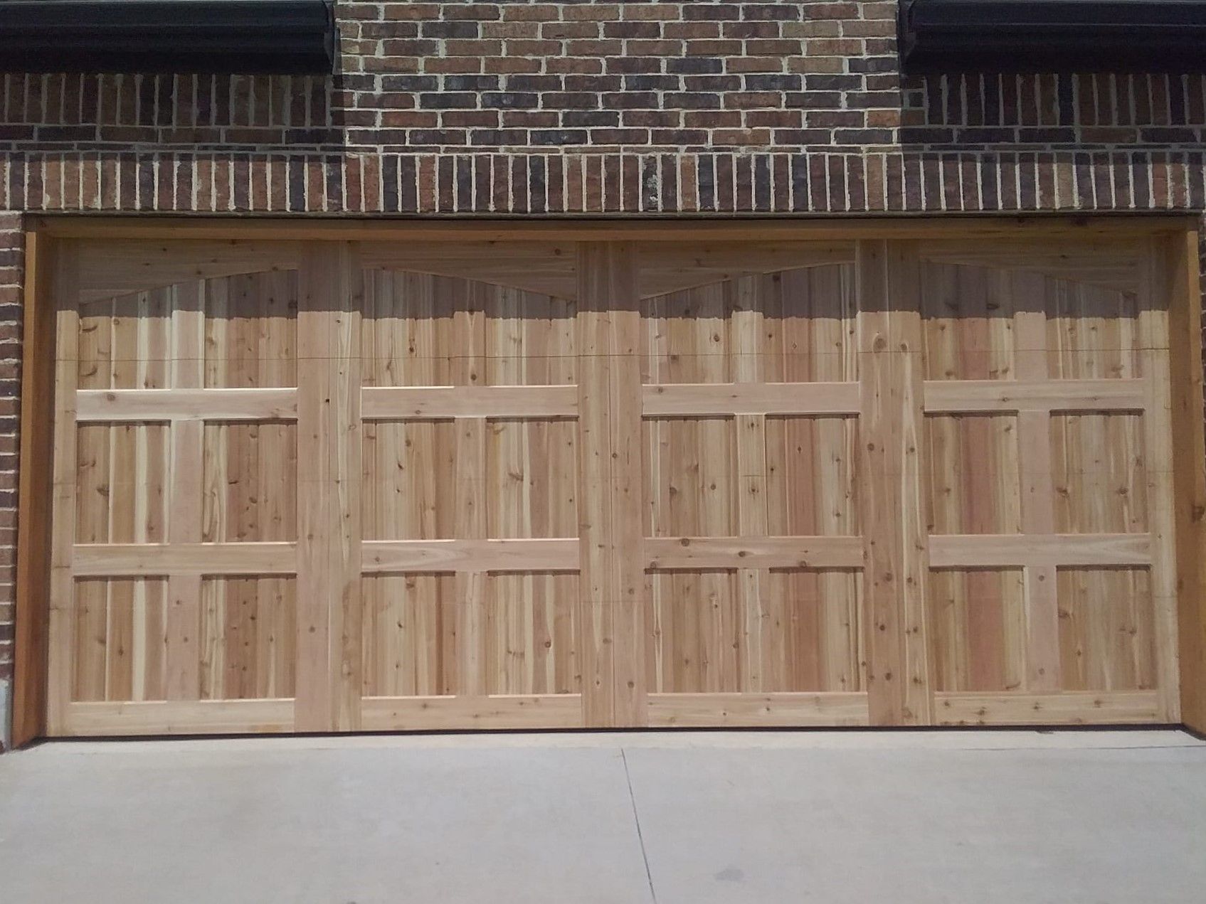 A wooden garage door with a grid panel design installed in a brick house exterior.