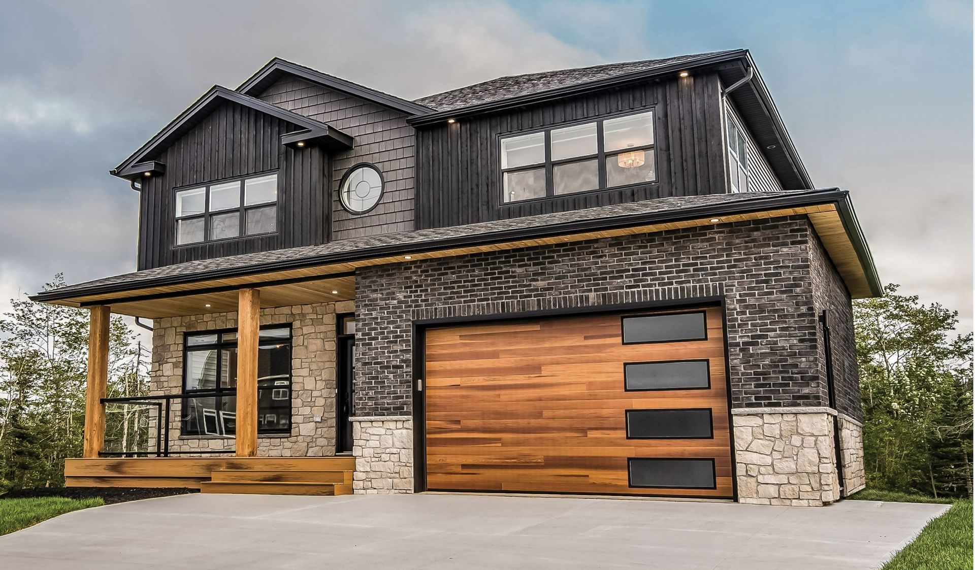 A modern two-story suburban house featuring dark vertical siding, stone masonry, a natural wood garage door, and a porch.