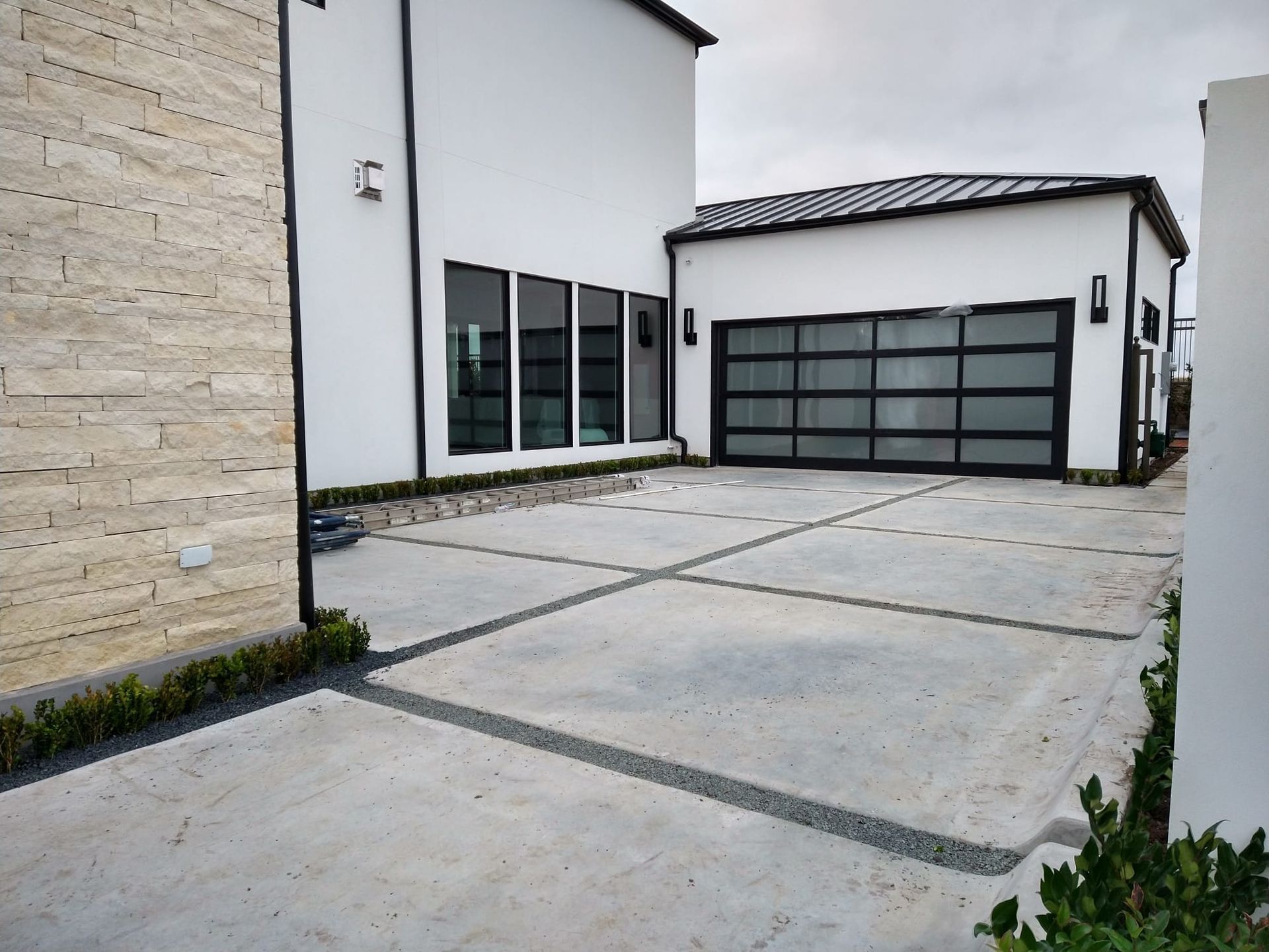 A modern house with a beige stone wall, white exterior, and a large multi-panel garage door beside a paved driveway.