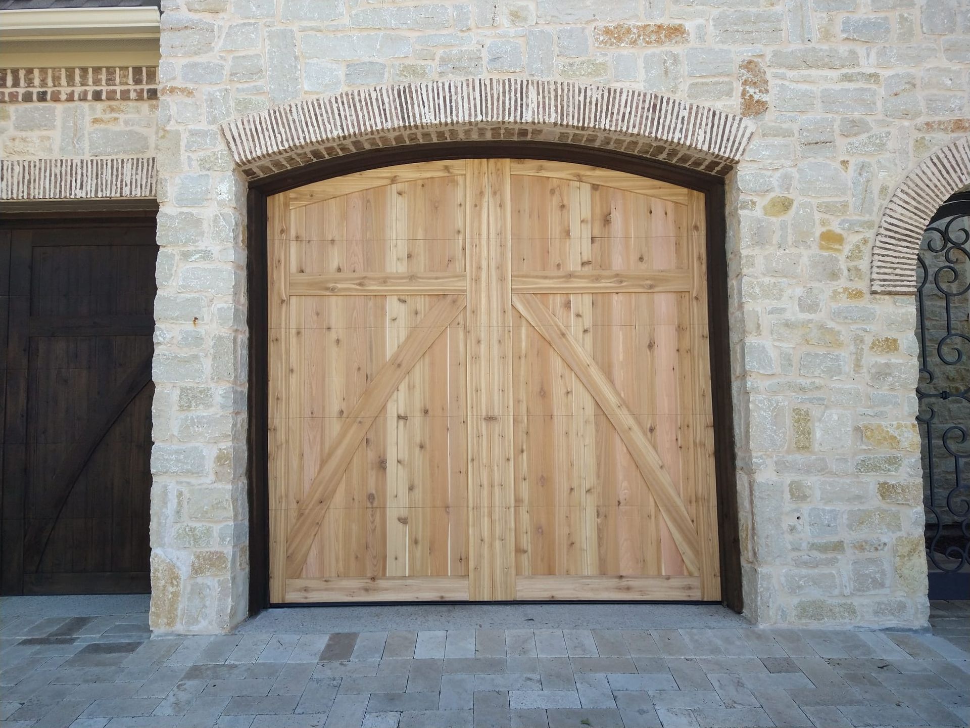 A wooden arched garage door set in a light-colored stone wall, with a smaller dark wooden door visible to the left.