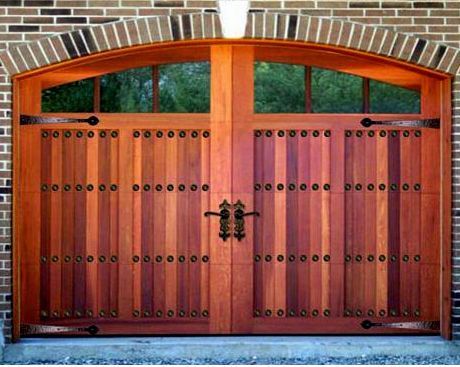 Arched wooden garage door with vertical planks, decorative iron hinges, and a central handle, set in a brick wall.