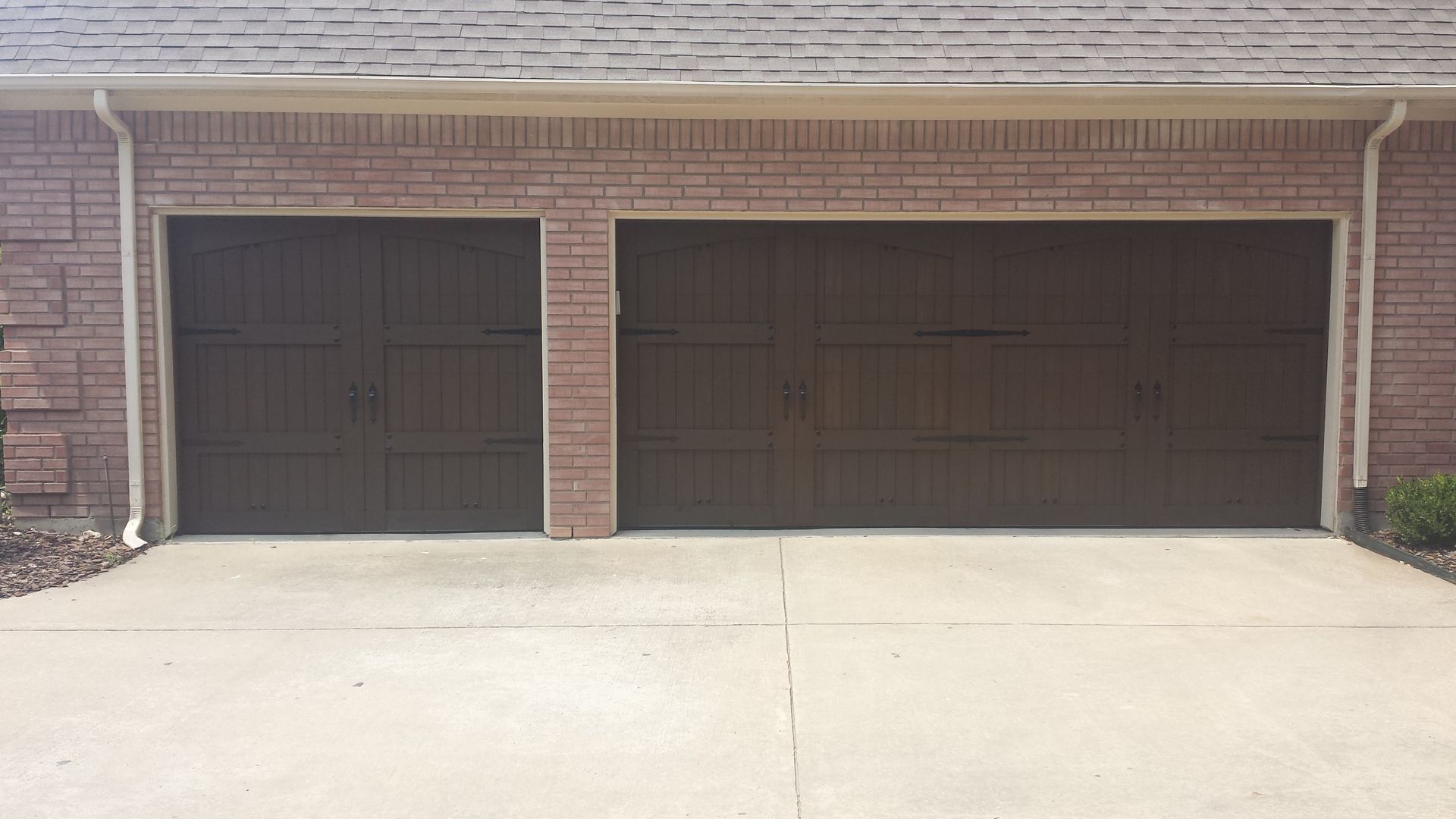 A brown, two-bay garage with matching panelled doors set into a red brick house with a concrete driveway.
