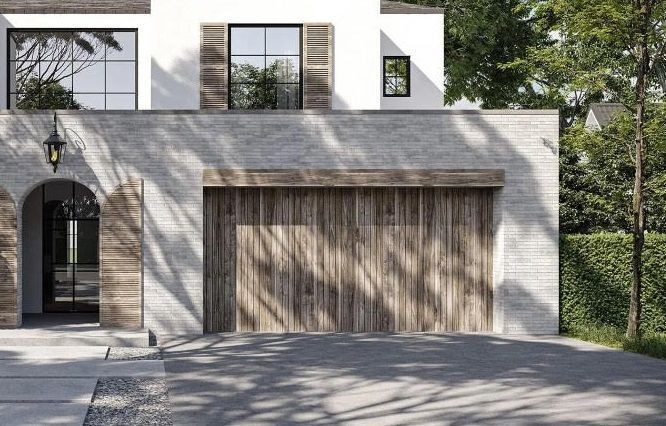 A modern home with white upper walls, light stone exterior, a wooden garage door, and an arched entryway.