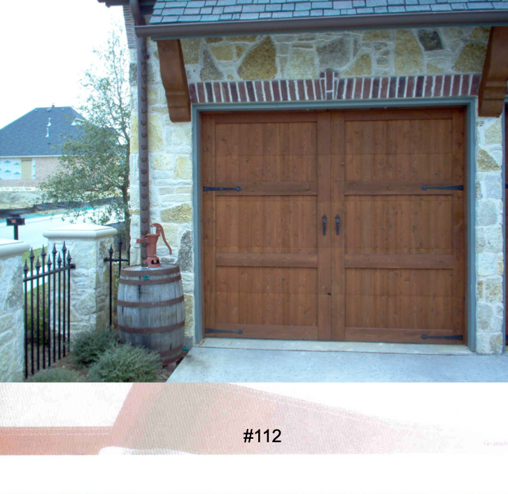 A rustic wooden garage door on a stone house exterior, with a vintage water pump on a barrel in the foreground.