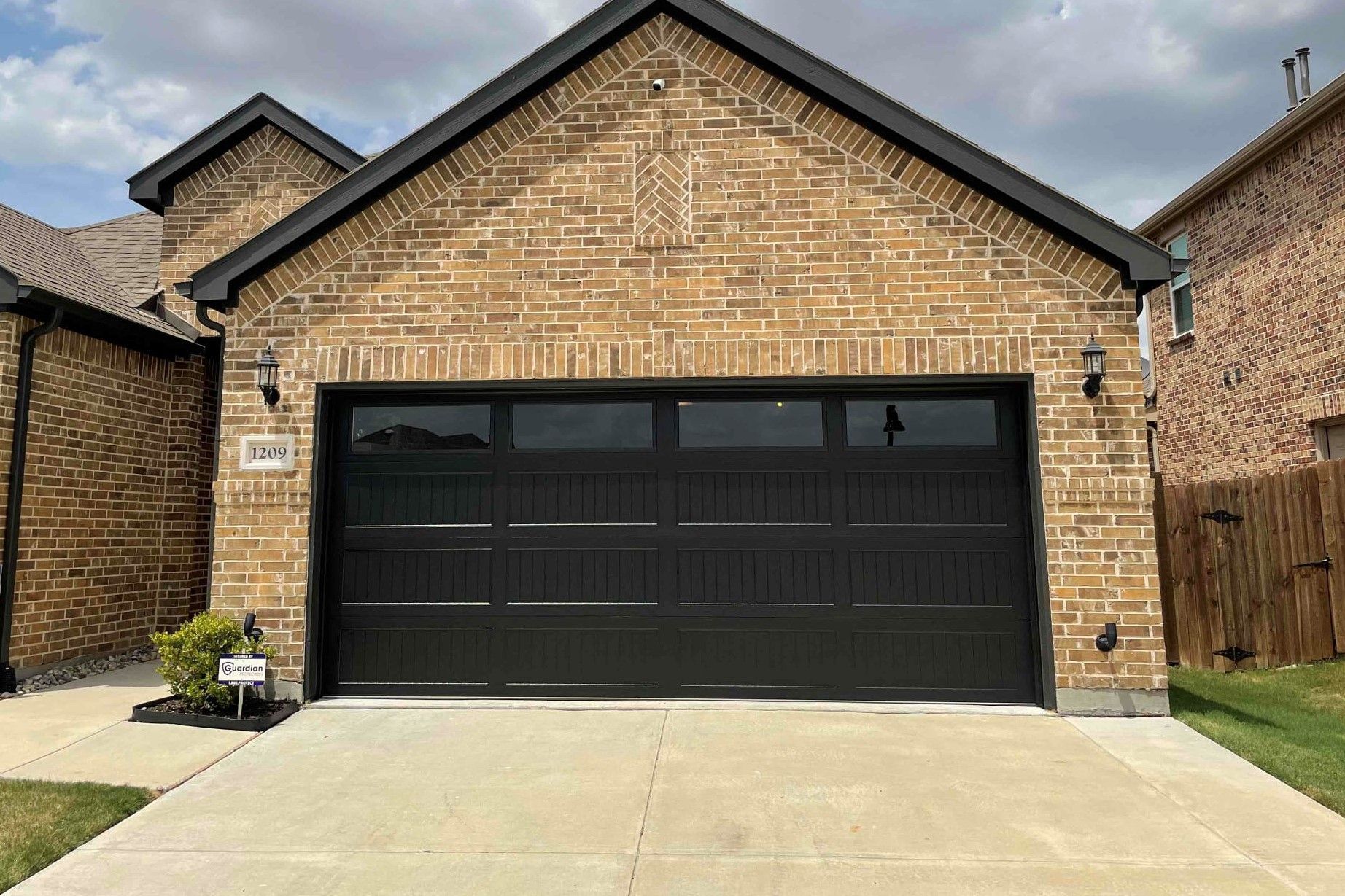 A residential brick house exterior featuring a dark brown, multi-paneled garage door with a row of upper windows.