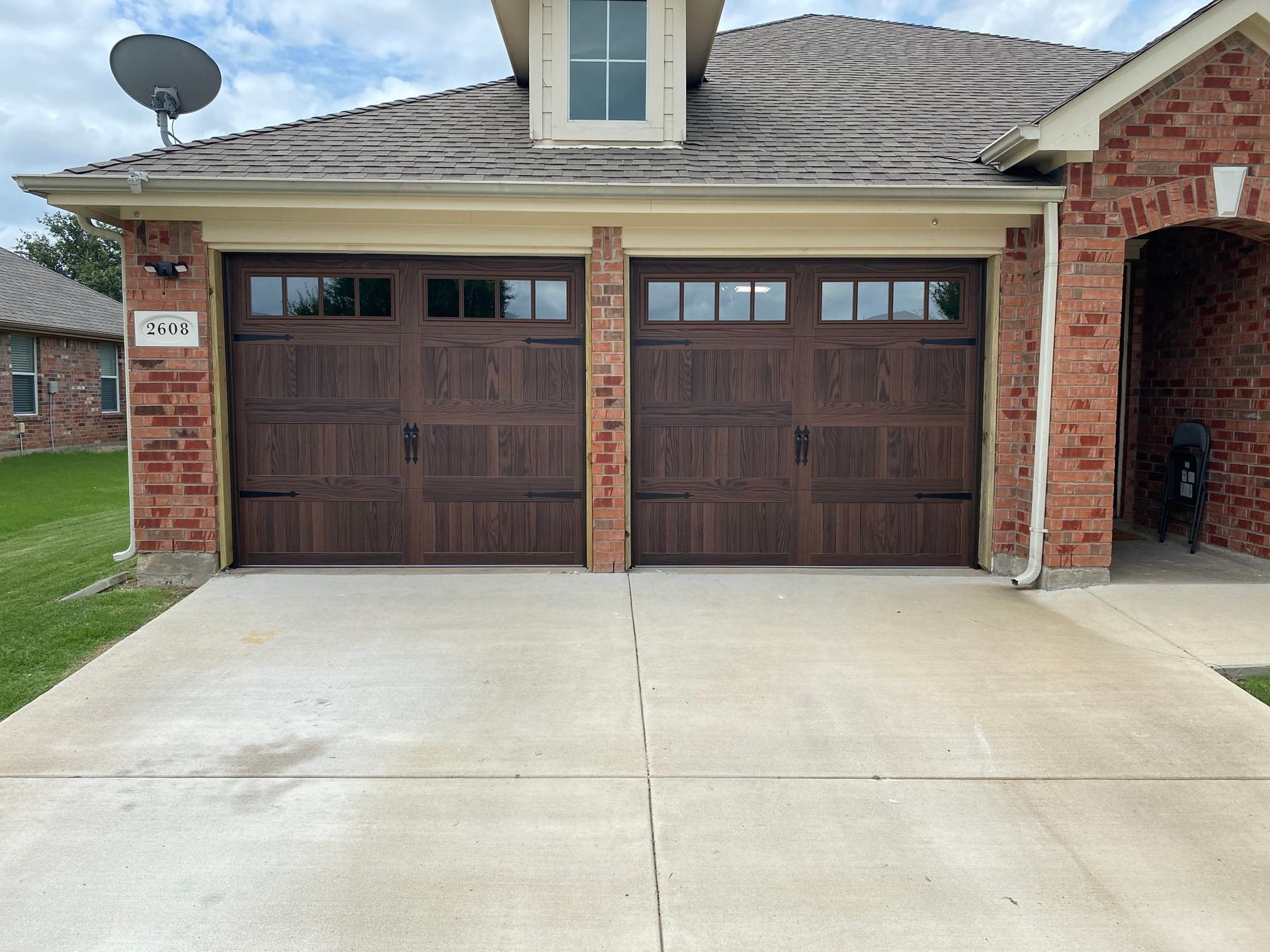 A two-car garage with dark brown paneled doors and small windows, set in a red brick house with a concrete driveway.