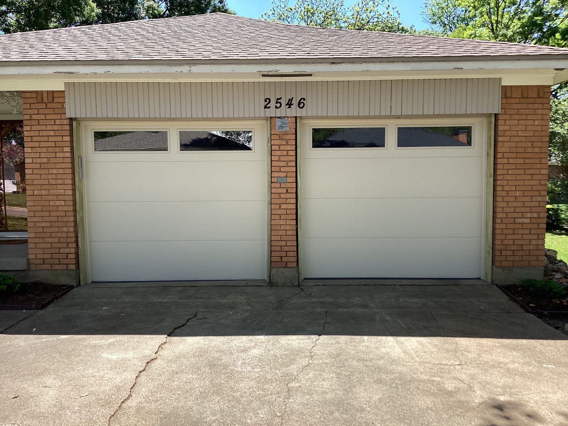 A brick garage exterior with two white doors, each featuring windows at the top and the address number 2646 above them.