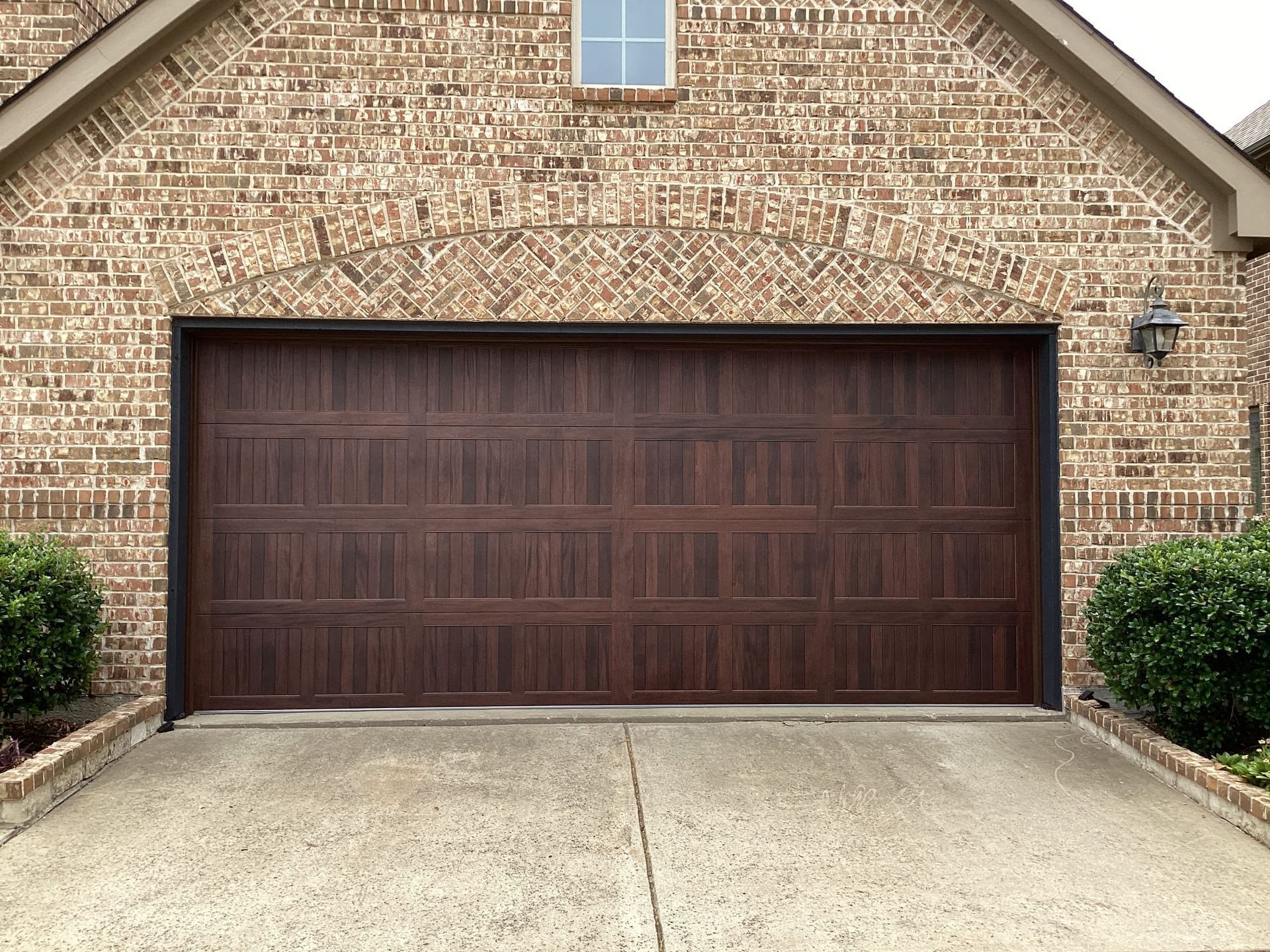 A dark brown, multi-paneled garage door installed in a brick house exterior, viewed from a concrete driveway.