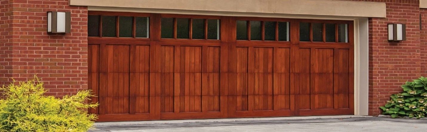 A wooden garage door with windows, flanked by brick walls and bushes.