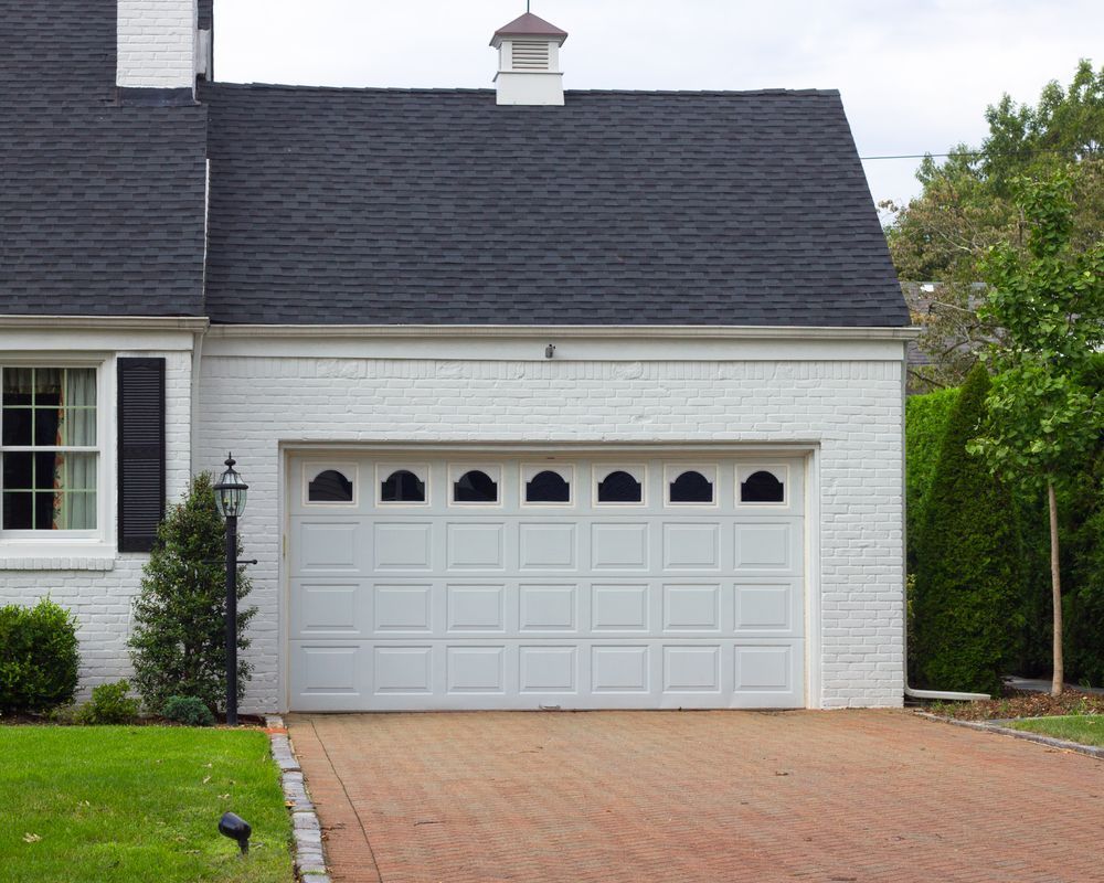 White brick house with a white garage door, black roof, and brick driveway.