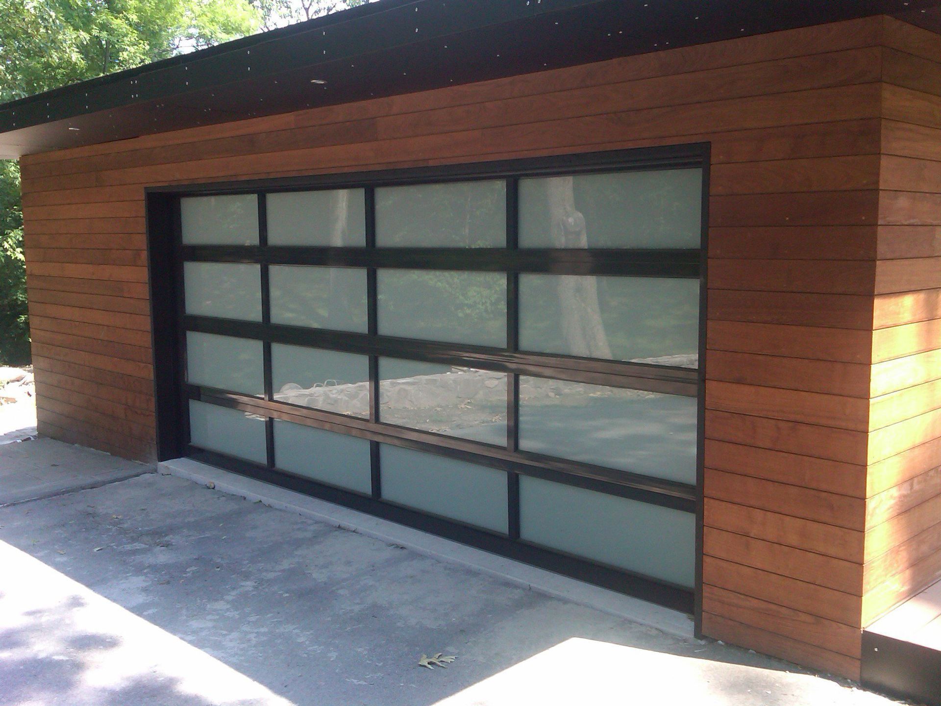 Modern garage with horizontal wood siding and a black-framed glass garage door with frosted panels.
