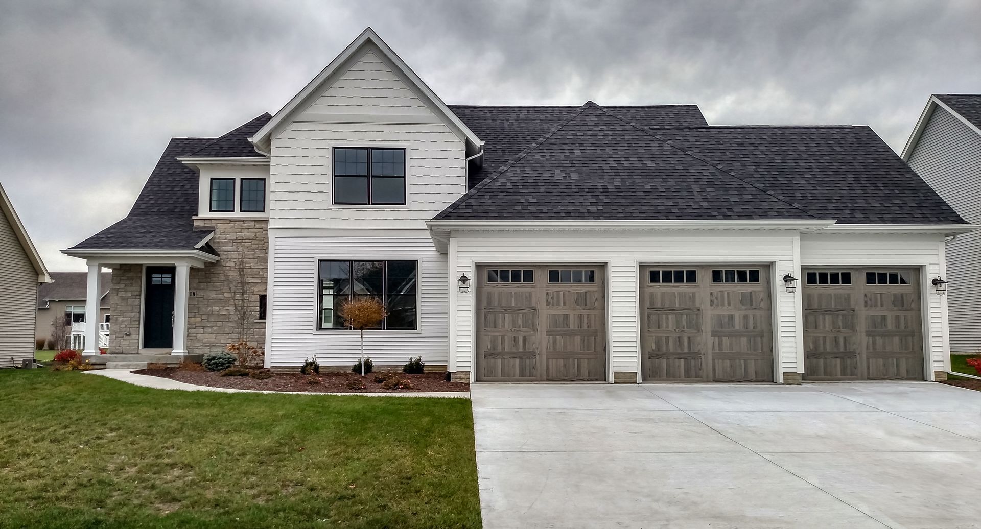 A two-story suburban house with white siding, stone veneer, dark gray roof shingles, and a three-car garage.