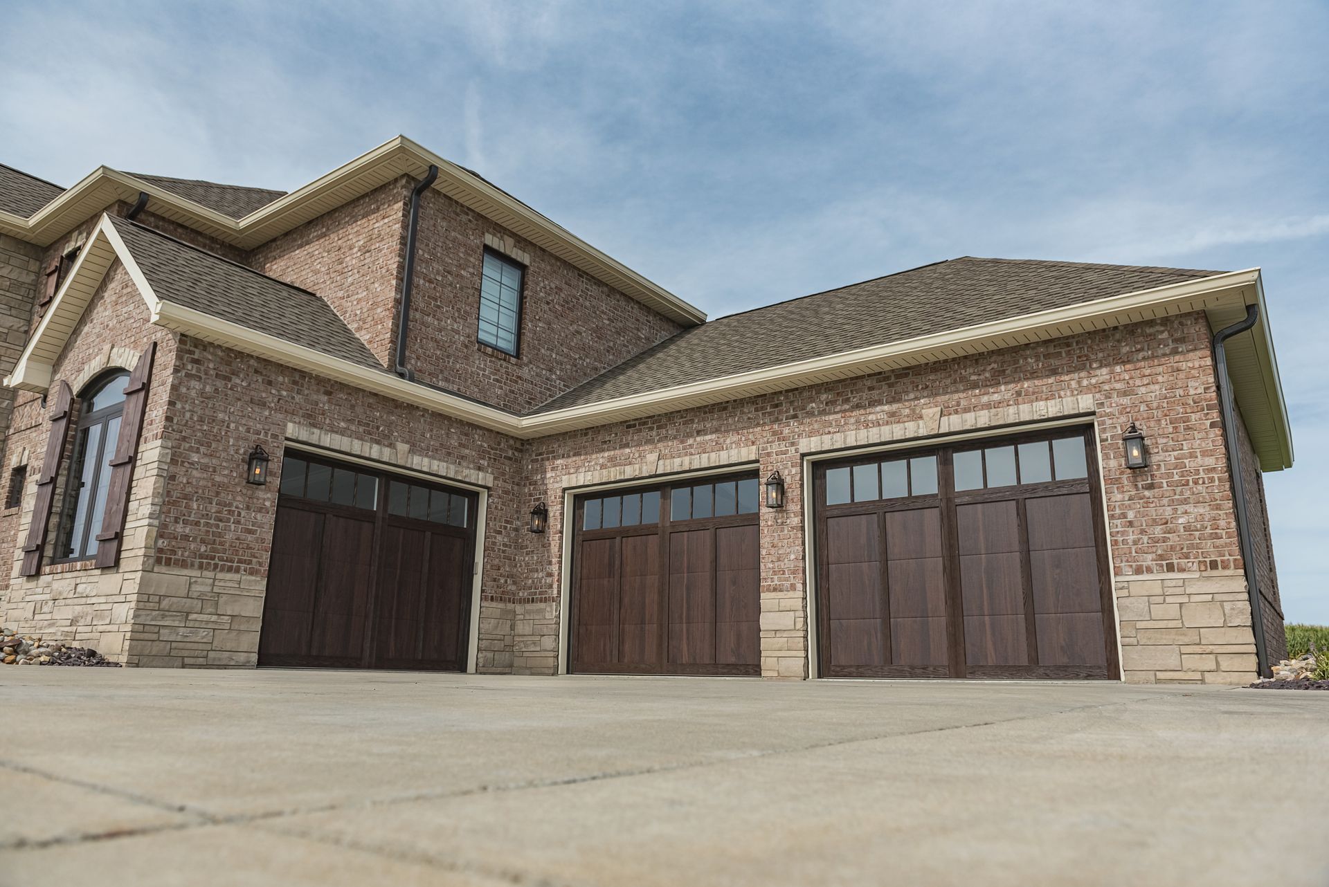 A tan brick house with three dark wood garage doors under a light blue sky.