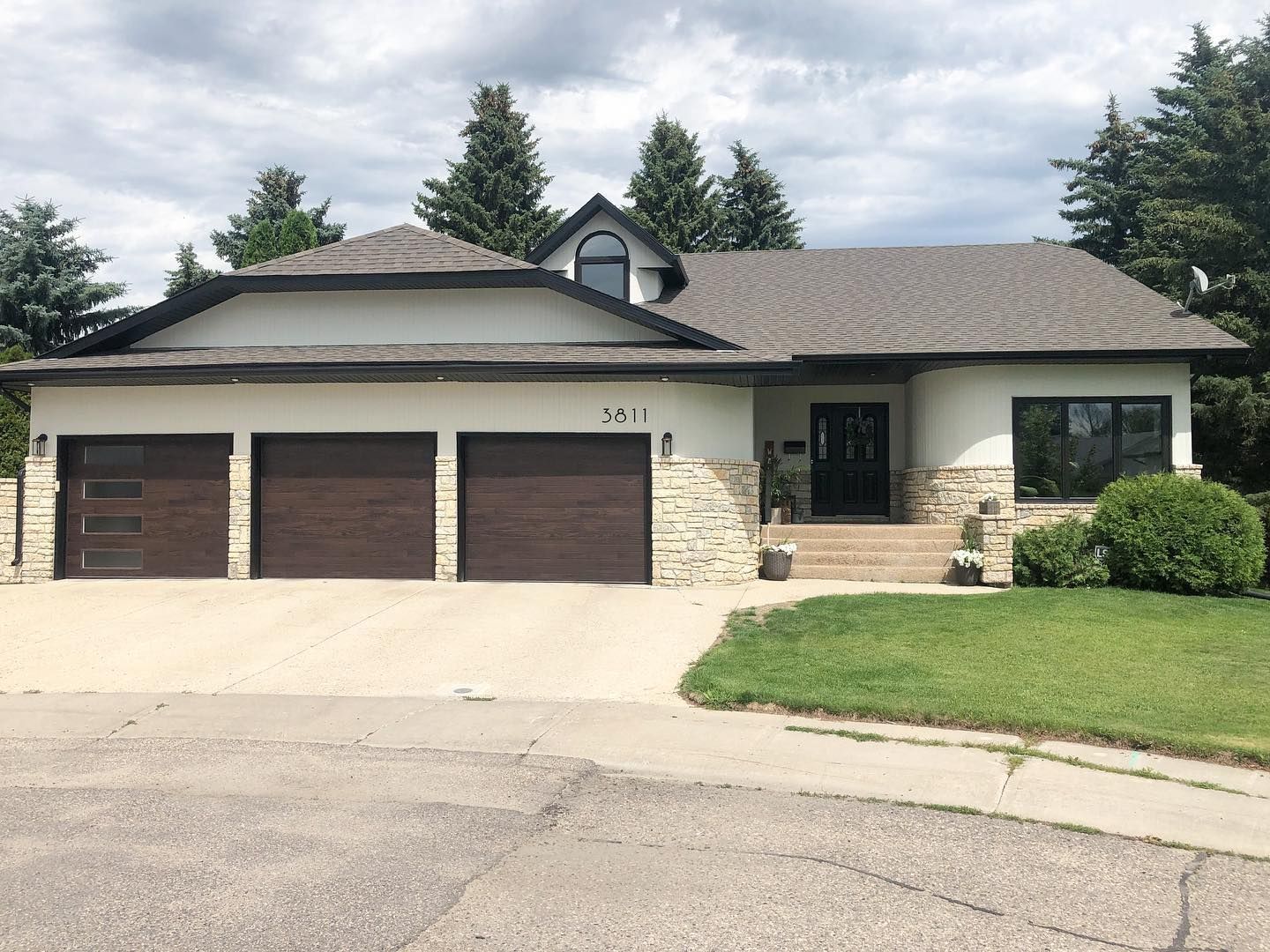 A suburban one-story house with a three-car garage, white stucco walls, stone accents, and a dark shingled roof.
