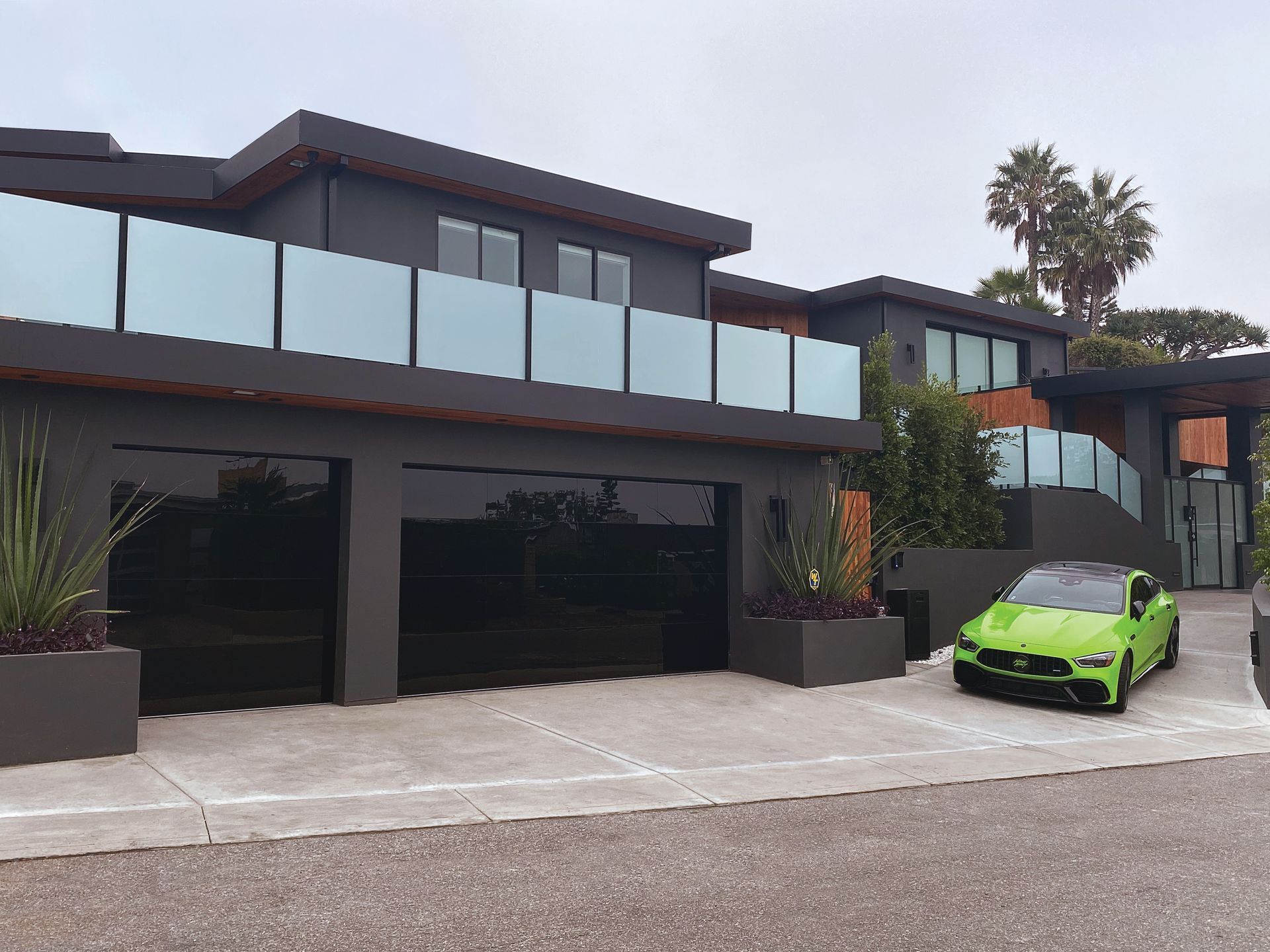 A modern two-story gray house with black garage doors and a bright green sports car parked in the driveway.