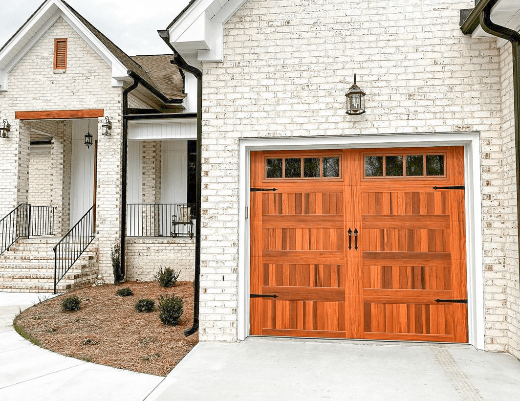 A white brick house exterior featuring a wooden garage door with windows and decorative iron hinges.