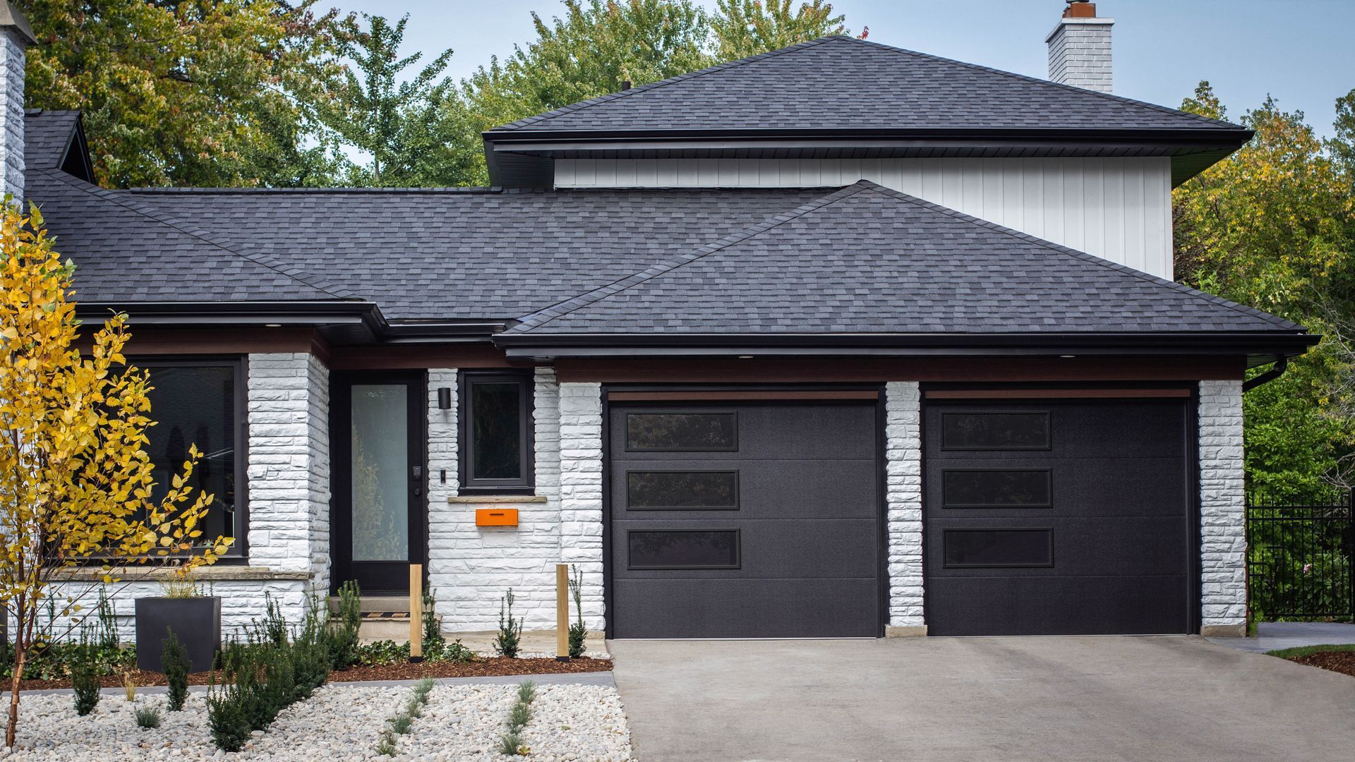 A single-story home with a black roof, white stone siding, and two black garage doors with horizontal window inserts.