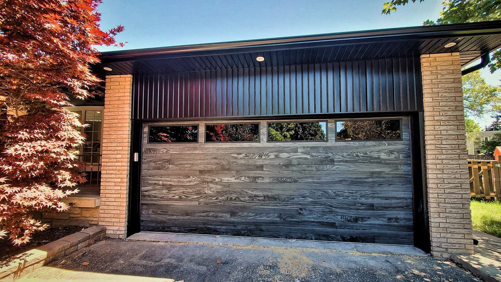 A garage with a rustic, gray-washed wood door, black corrugated upper siding, and textured light-stone side columns.