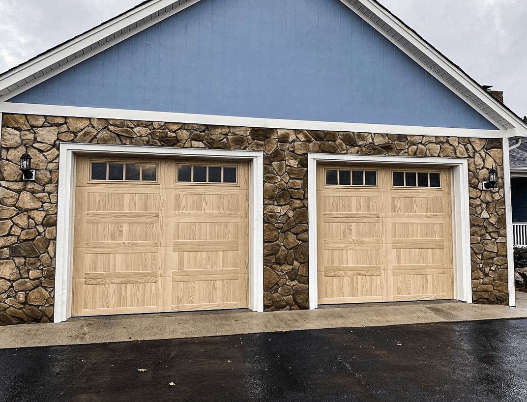 A blue garage with stone exterior siding and two light-colored wooden garage doors with small rectangular windows.