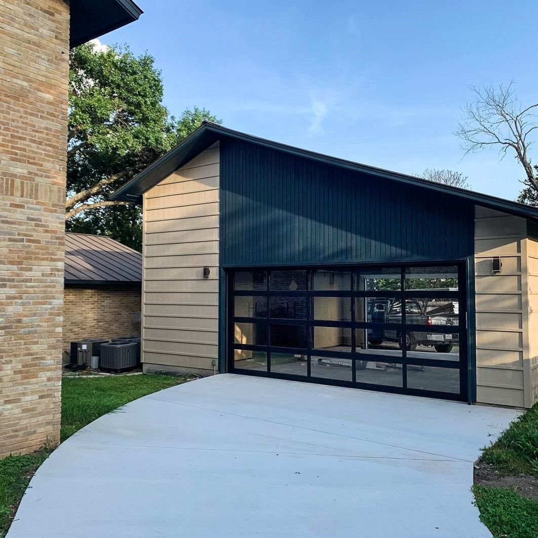 Modern garage with horizontal wood-slat siding, a dark metal upper section, and a large, multi-panel glass door.