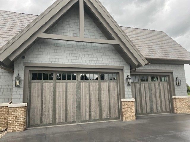 A two-car garage with wood-grain doors, grey shingle siding, and stone accents under a gabled roof.