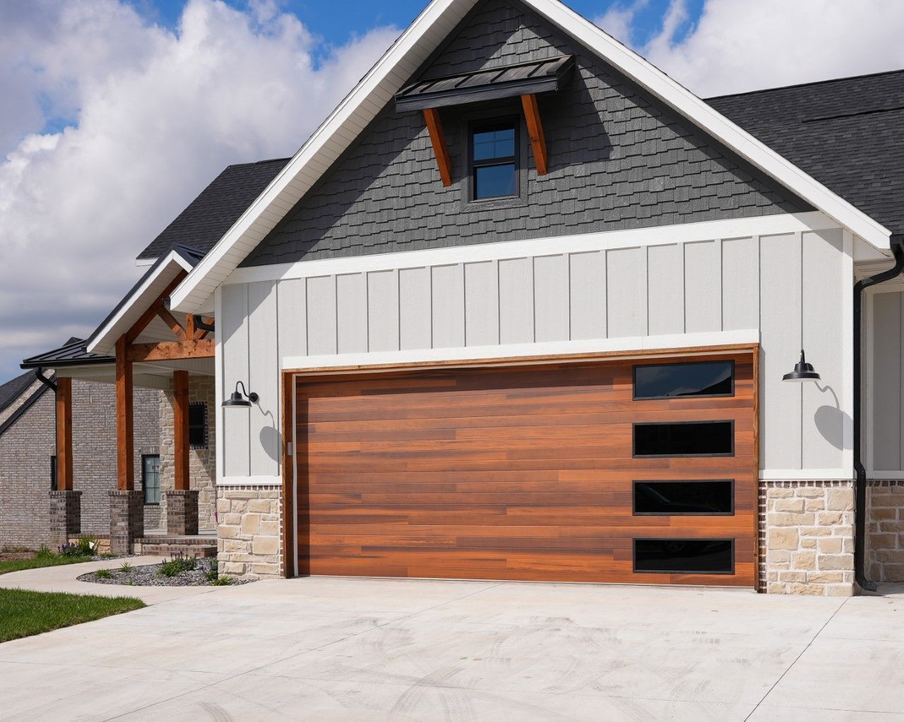 Modern house exterior with a wood-look garage door featuring a vertical row of four windows, under a grey gable roof.