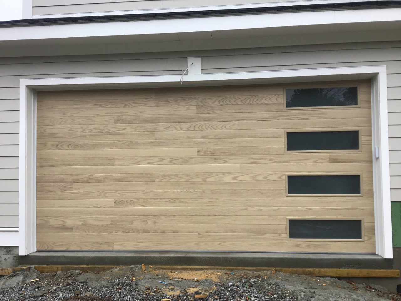 Modern wooden garage door with four rectangular windows vertically aligned on the right side.