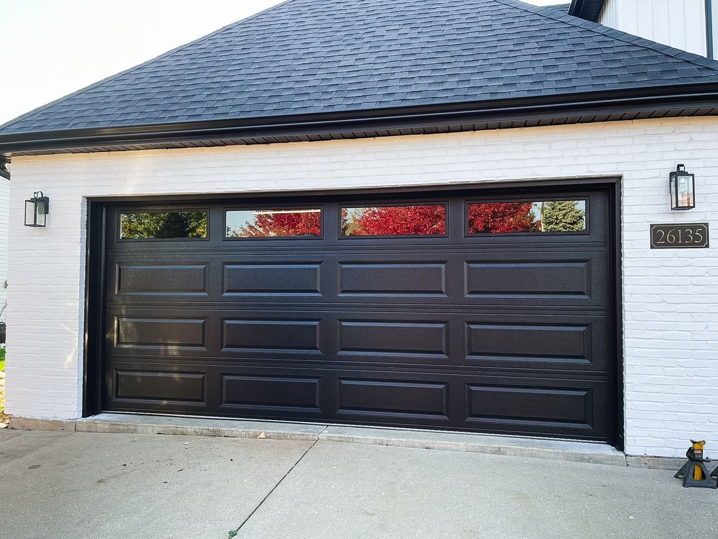 A black, four-panel residential garage door with rectangular windows, set into a white brick exterior wall.