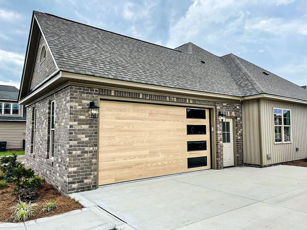A brick house exterior featuring a light-wood tone, modern garage door with vertical windows, and a paved driveway.