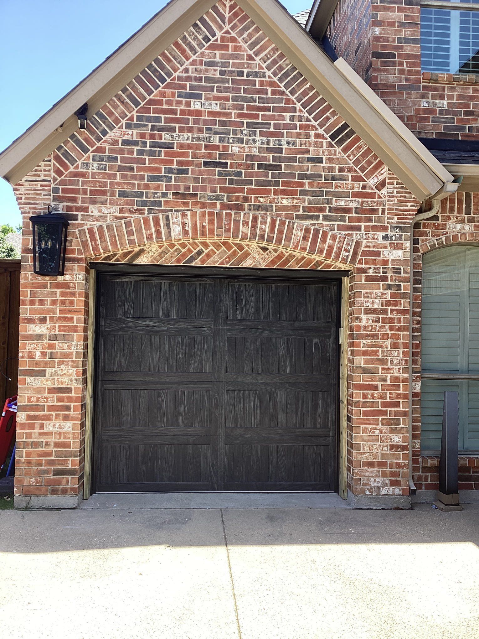 A brick house exterior featuring a weathered, dark brown garage door under a decorative brick archway.